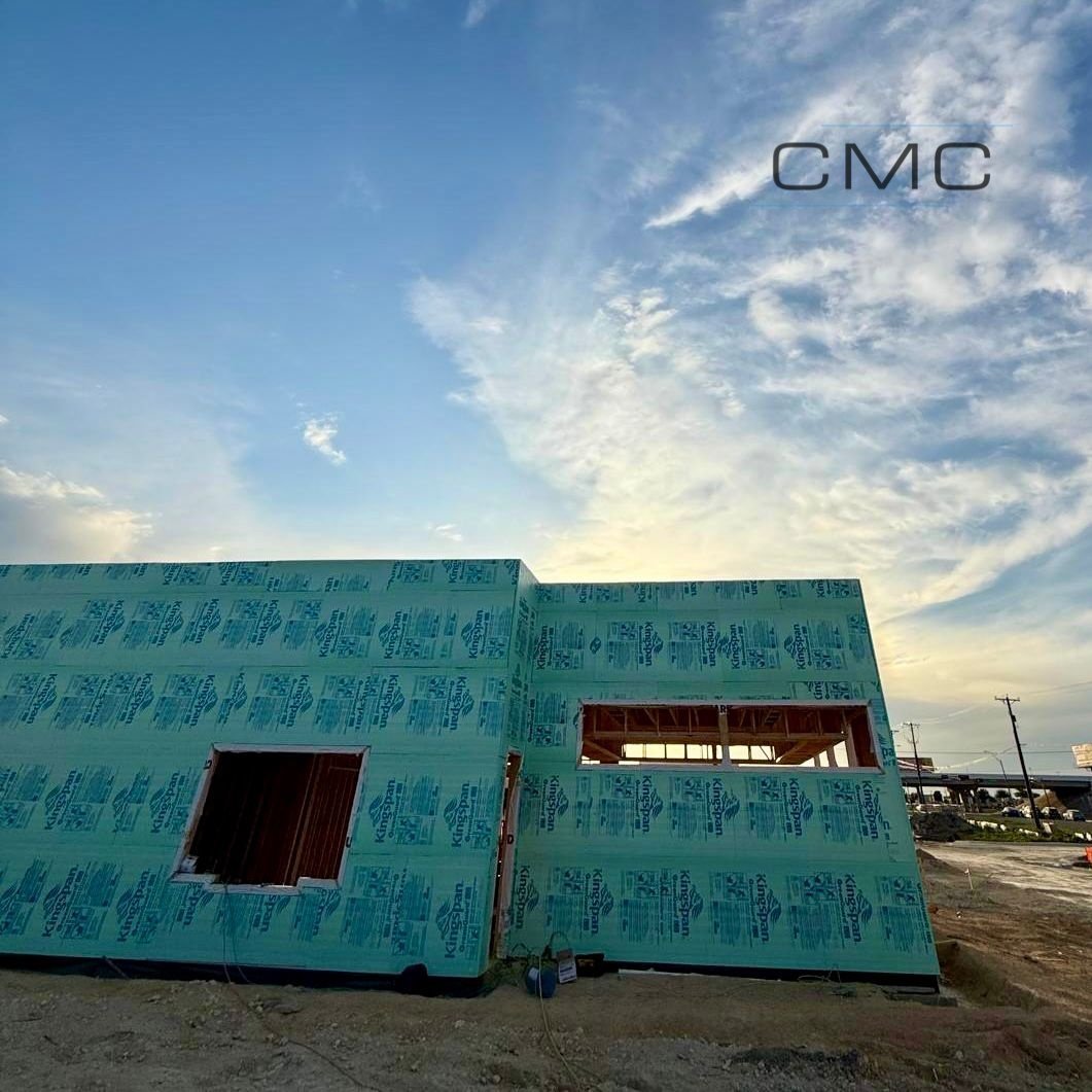 Construction site with turquoise insulation-wrapped building frame under blue sky with white clouds