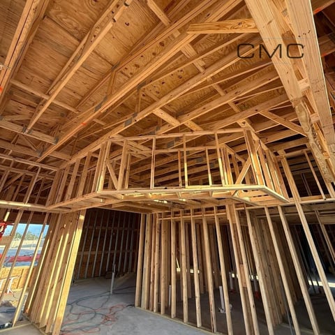 Interior of a wood-framed house under construction showing exposed wooden beams and wall framing
