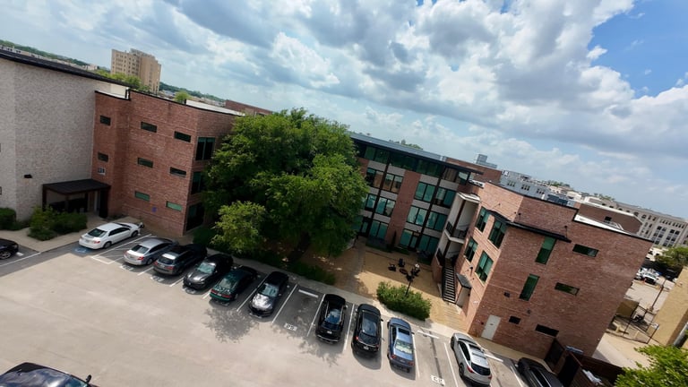 Parking lot with multiple vehicles in front of red brick industrial buildings under a partly cloudy sky