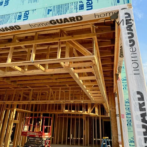 Wooden house framing under construction with blue and white HomeGuard house wrap covering the roof and walls