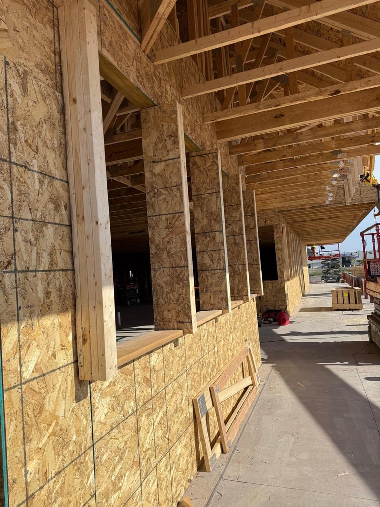 Interior of a home under construction showing wooden framing, OSB sheathing, and exposed studs along a hallway