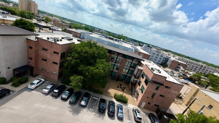 Aerial view of urban residential area with brick buildings, parking lot with cars, green trees, and cloudy sky
