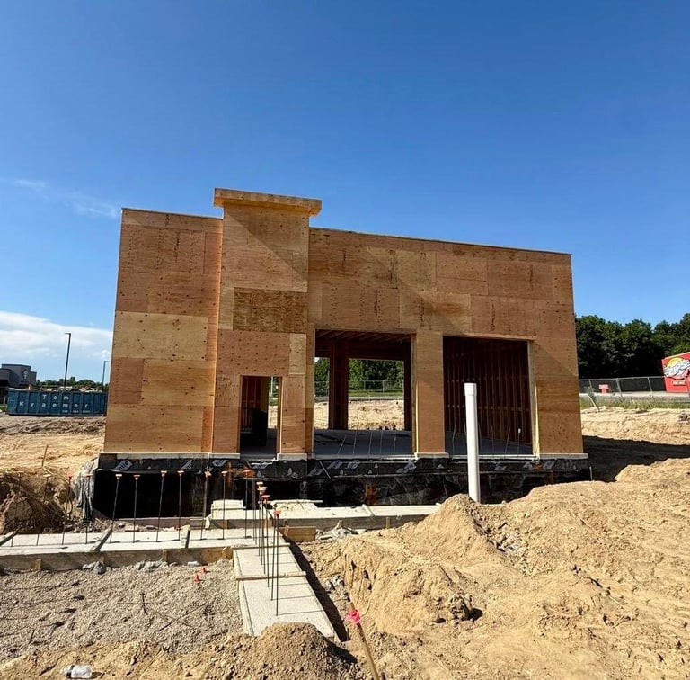 New home under construction with wooden frame and brick exterior on foundation, surrounded by dirt and construction materials