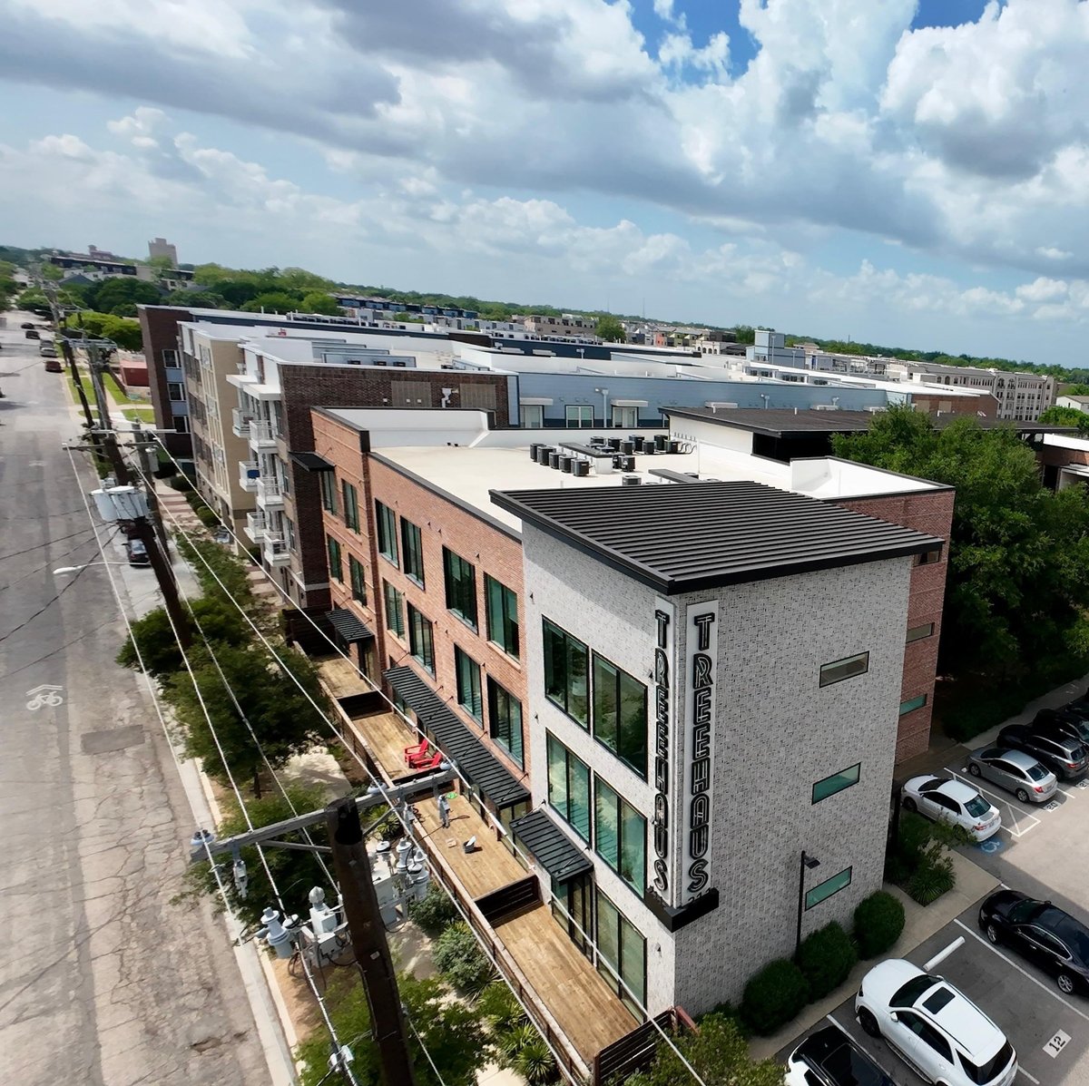 Aerial view of modern mixed-use buildings with solar panels on roofs, parking area, and green landscaping in suburban development