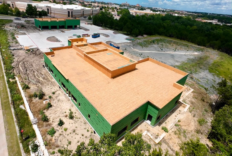 Aerial view of industrial building with green walls and wooden roof structure under construction on a hillside site