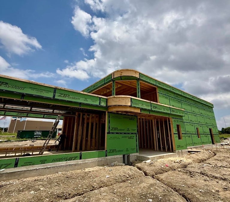 Green and brown industrial building under construction on a dirt lot with blue sky and clouds