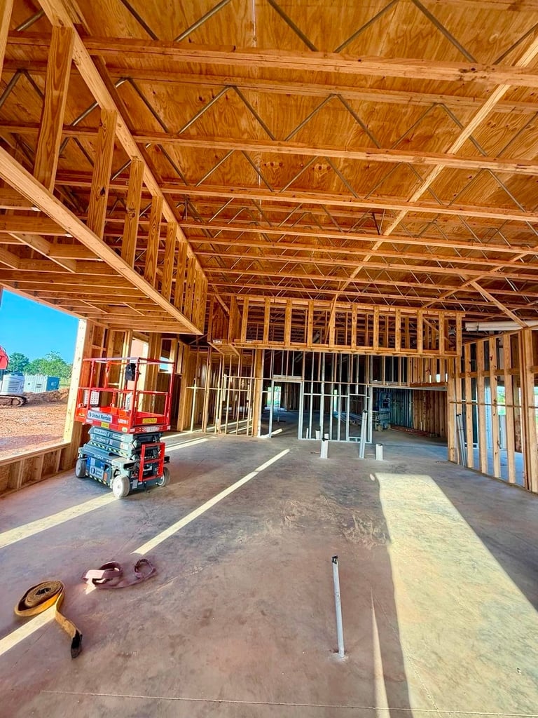 Interior of a residential home under construction showing exposed wooden framing, concrete floors, and construction materials.