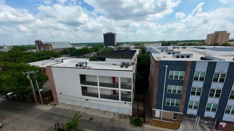 Aerial view of modern residential buildings in an urban neighborhood with green spaces and downtown skyline in the background