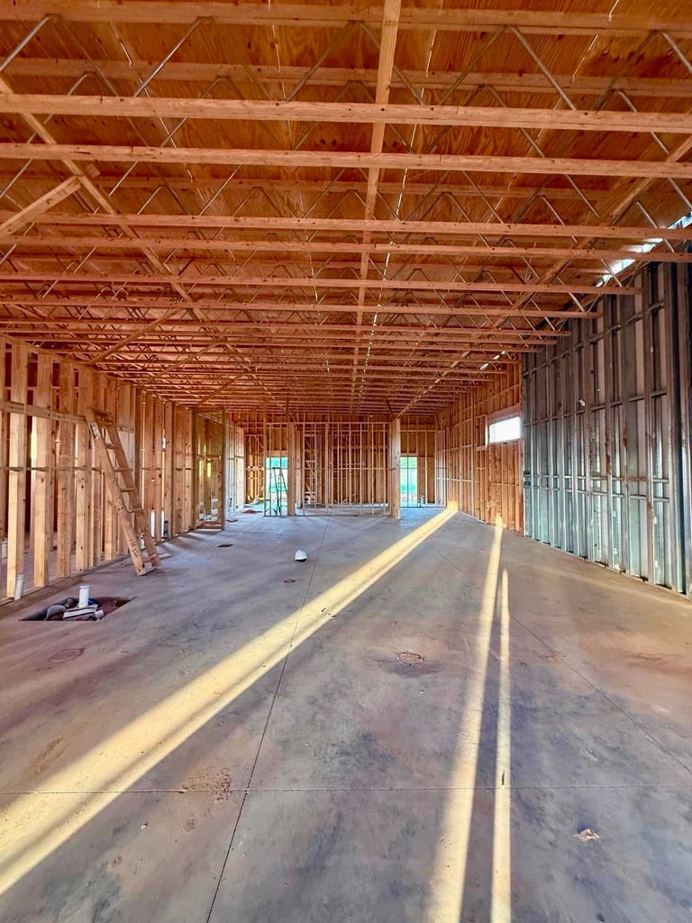 Interior of an unfinished commercial building with wooden framing, exposed ceiling beams, and concrete floor under construction.