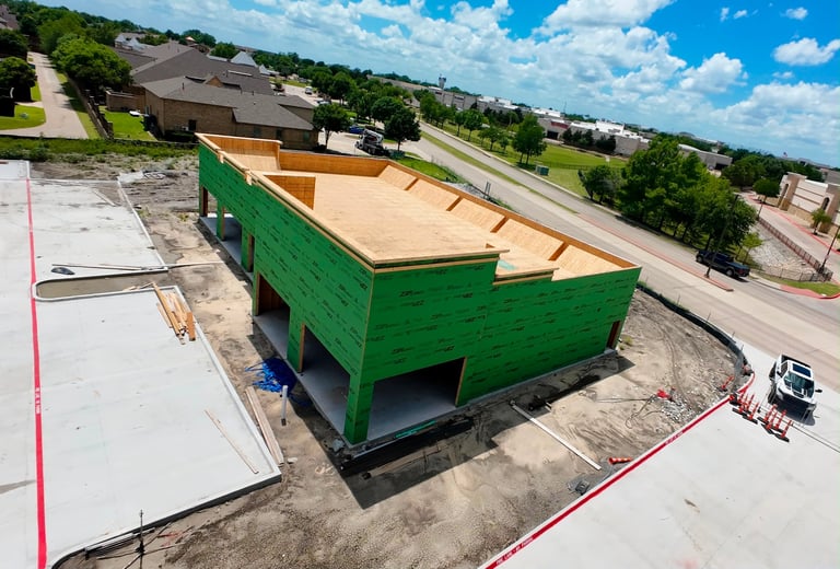 Large green metal dumpster bin on residential construction site with houses and trees in background