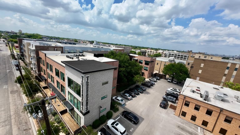 Aerial view of a residential urban neighborhood with multi-story apartment buildings, parked cars, and cloudy sky